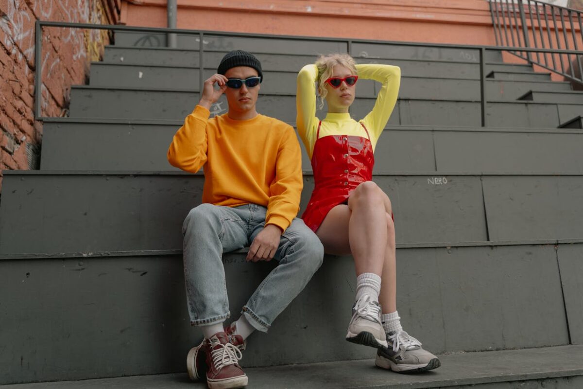 Trendy young adults in vibrant outfits and sunglasses sitting on industrial bleachers.